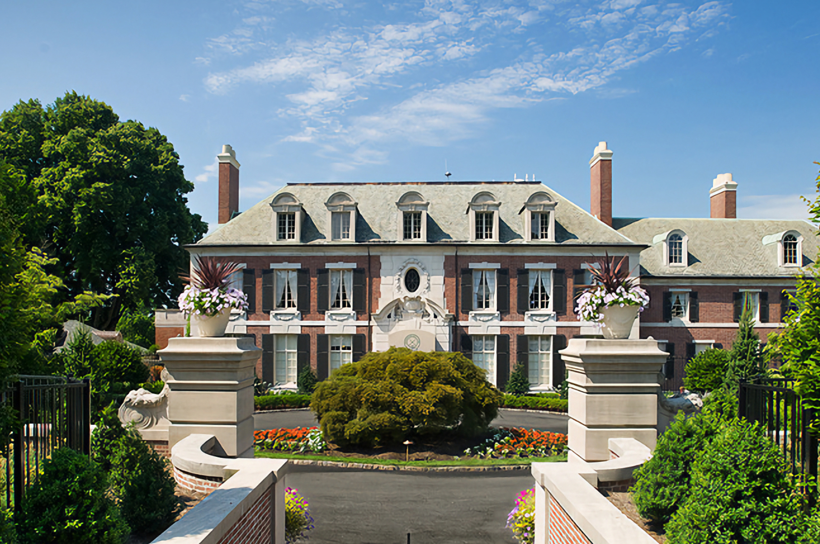 Brick manor with symmetrical windows, central arched entry, and surrounding formal garden.With planters flanking the path.