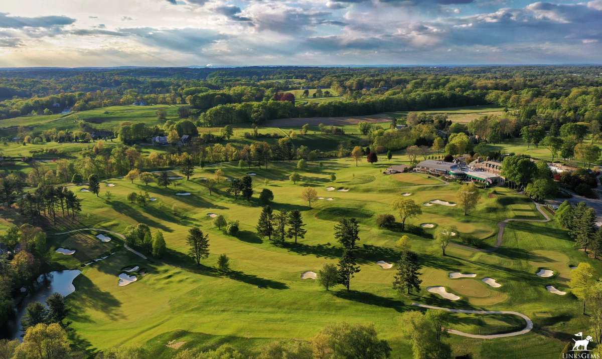 Aerial view of a expansive golf course with green fairways, multiple sand bunkers, and a clubhouse in the distance.