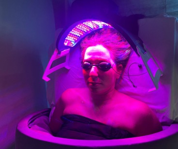 support2 | Petite Retreat Person reclining inside a tanning bed under purple UV light, wearing protective sunglasses.